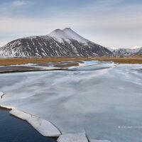Blick von der Ringstraße Hringvegur auf den im Winter teils vereisten Gletscherfluss Hoffellsá mit dem Berg Gjánúpshorn im Hintergrund im frühen Morgenlicht Islands.