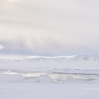 Die Sonne bescheint durch dichten Hochnebel kleine vereiste Seen zwischen Bergen im Hochland Islands.