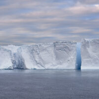 Ein Tafeleisberg, in drei Teile gebrochen unter rosa Schäfchenwolken am Morgen.