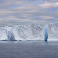 Ein Tafeleisberg, in drei Teile gebrochen unter rosa Schäfchenwolken am Morgen.