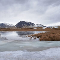Eine typische Winterlandschaft auf der Halbinsel Snæfellsnes mit eisbedekten Wasserflächen im Vordergrund und beschneiten Bergen am Horizont.