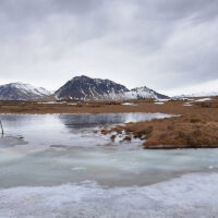 Eine typische Winterlandschaft auf der Halbinsel Snæfellsnes mit eisbedekten Wasserflächen im Vordergrund und beschneiten Bergen am Horizont.